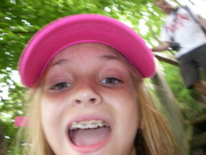 A pre-teen girl in a pink hat taking a selfie in the woods