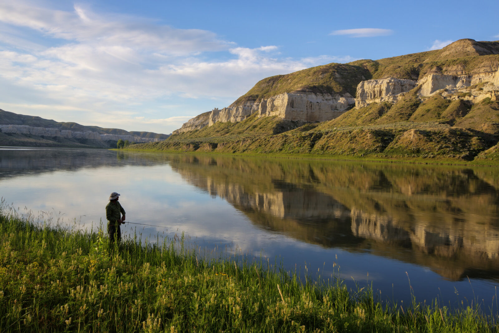 A photo of a fisherman along the river, with towering bluffs across the stream